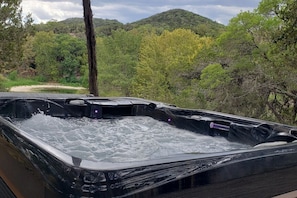 A hot tub in a natural setting with a view of a forested hill. - Madrona Casita | Romantic Stay w/ Hot Tub & Views (Pipe Creek)