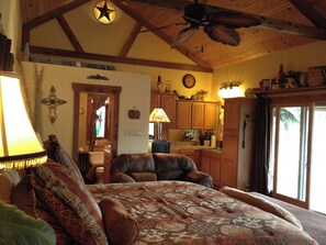 A cozy room with a bed, a chair, a lamp, and a ceiling fan. - Madrona Casita | Romantic Stay w/ Hot Tub & Views (Pipe Creek)