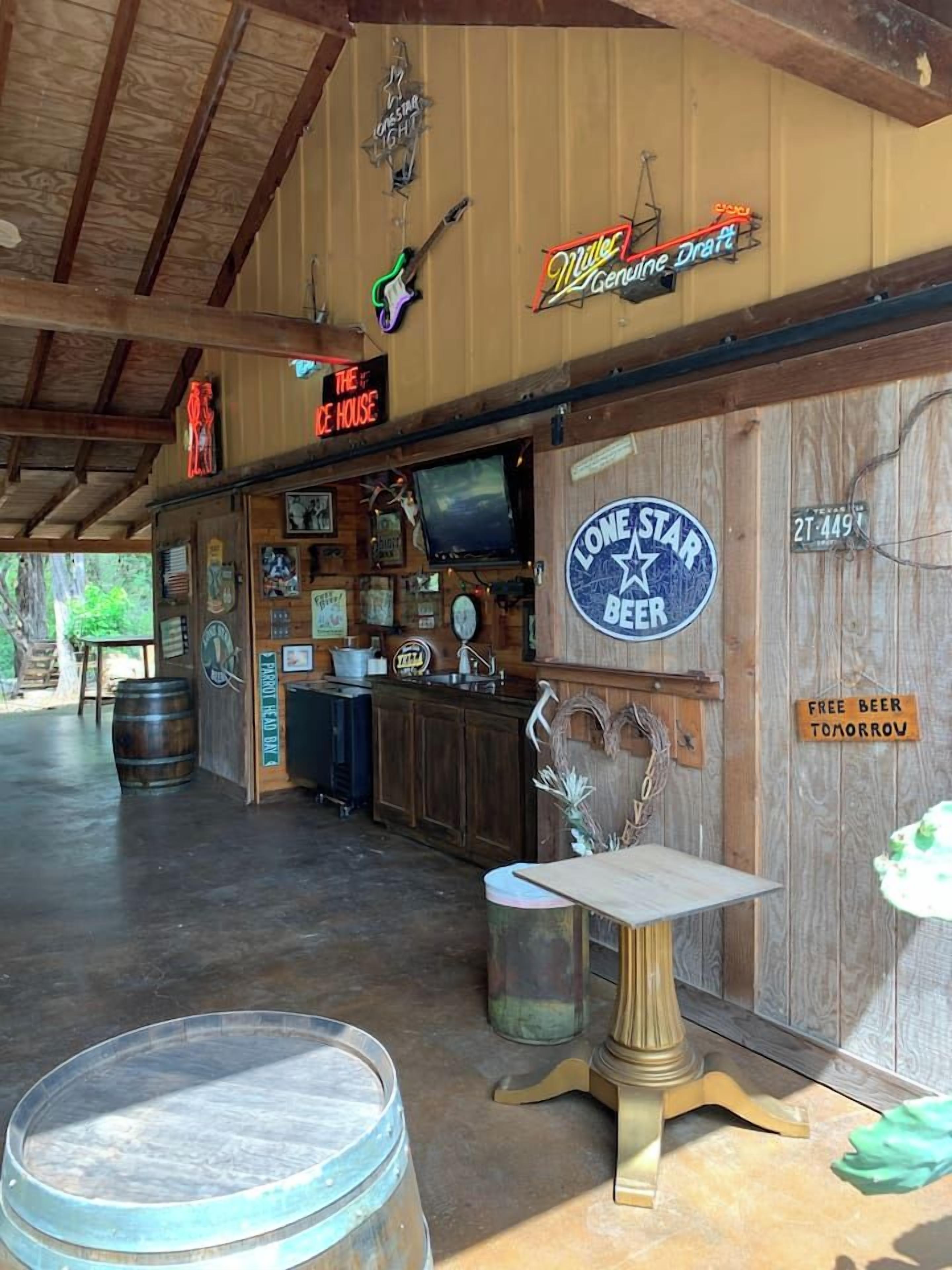Un coin bar au décor rustique, avec des murs en bois, un panneau néon représentant la marque de bière Miller Genuine Draft, un panneau représentant la marque de bière Lone Star, et un panneau indiquant « Bière gratuite demain ».