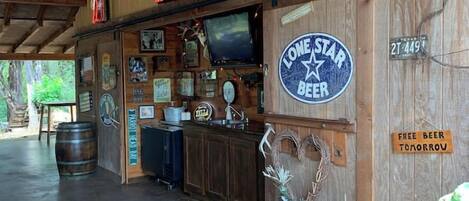 Un coin bar au décor rustique, avec des murs en bois, un panneau néon représentant la marque de bière Miller Genuine Draft, un panneau représentant la marque de bière Lone Star, et un panneau indiquant « Bière gratuite demain ».