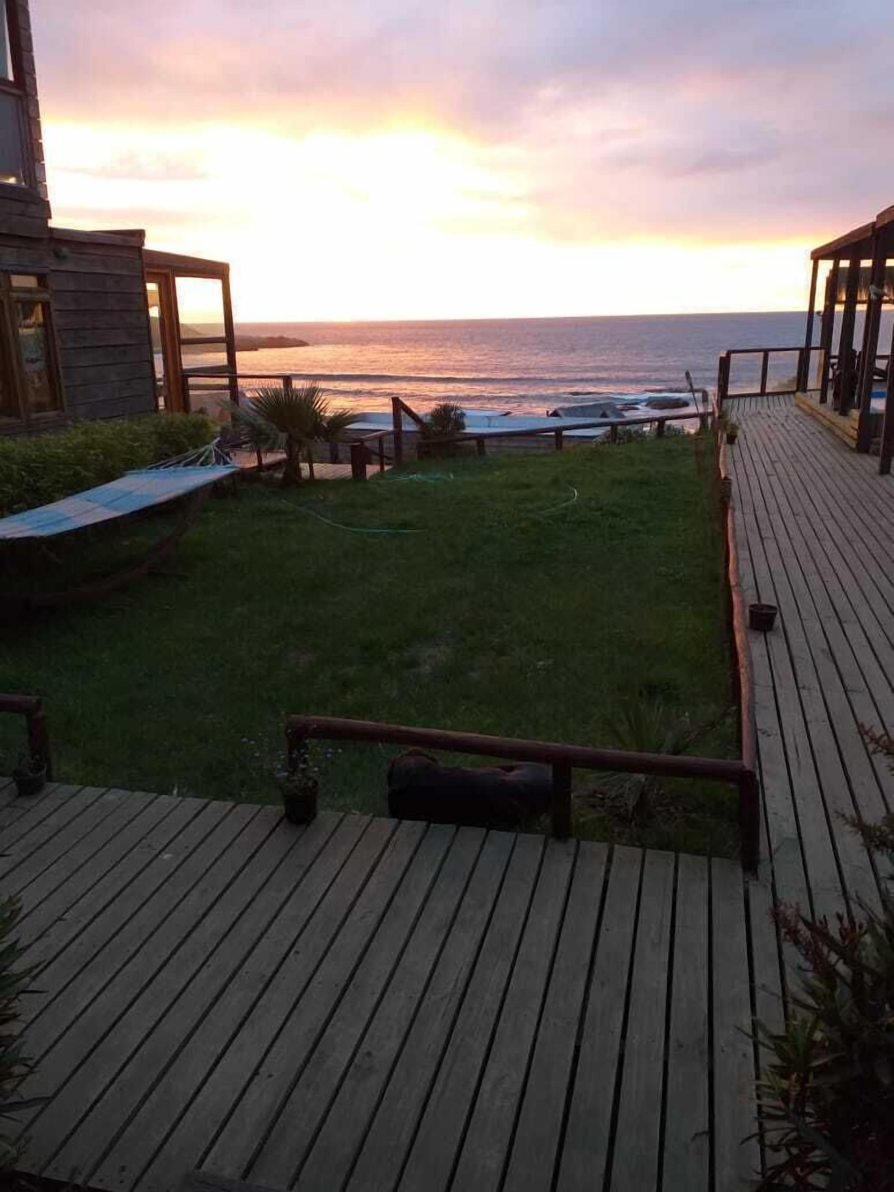A wooden deck with a grassy area and a view of the ocean at sunset.