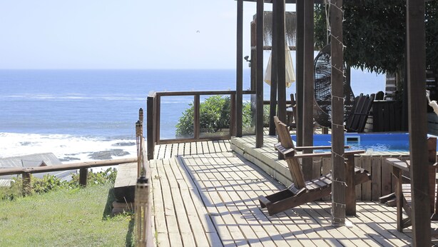 A wooden deck with a view of the ocean, a pool, and a covered seating area. - Ruka Antu Ecolodge (Cobquecura)