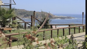 A wooden deck with a view of the ocean and hills. - Ruka Antu Ecolodge (Cobquecura)