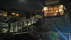 A modern building with a staircase leading to a lit interior, surrounded by greenery. - Ruka Antu Ecolodge (Cobquecura)