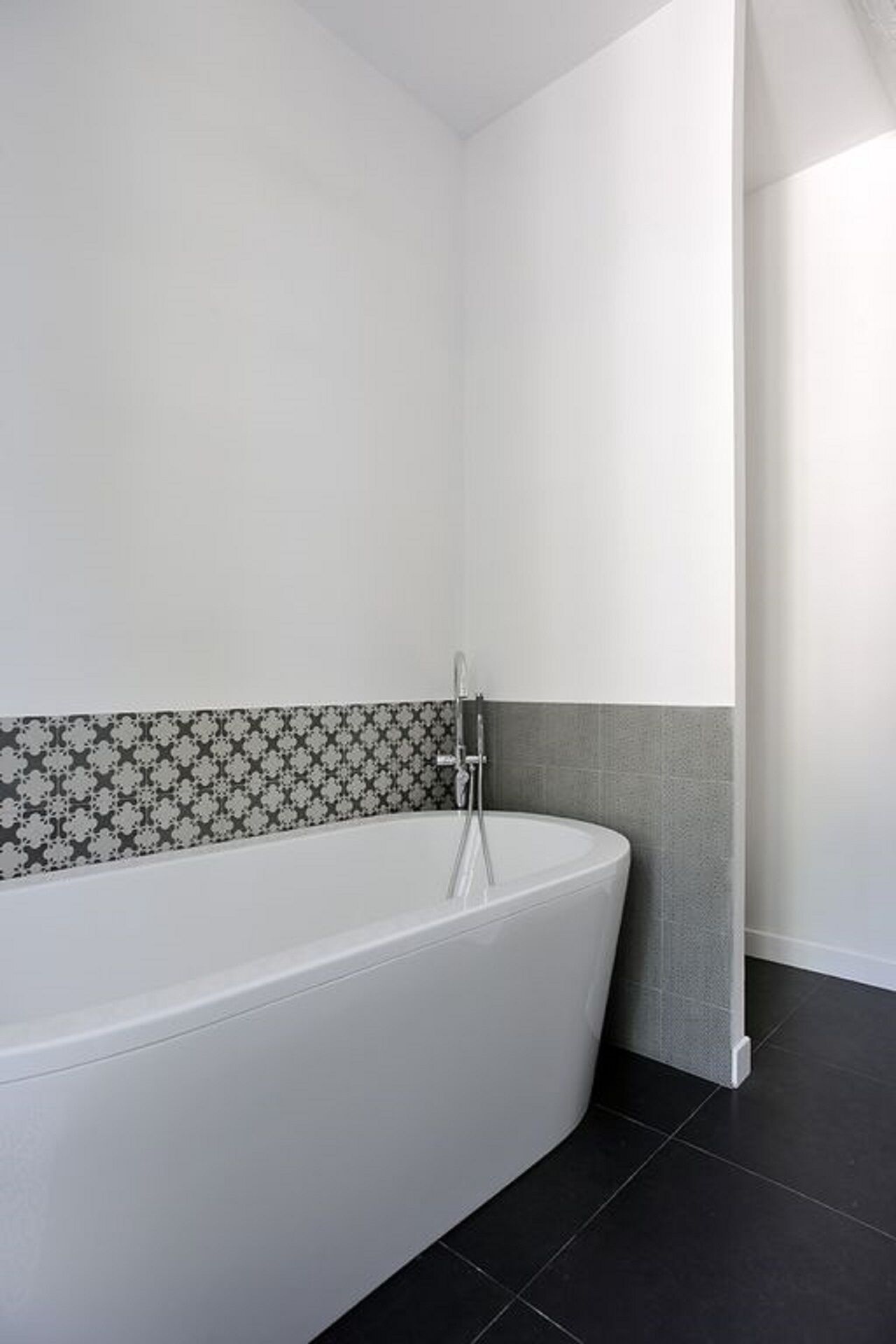 Un baño moderno con una bañera independiente, baldosas de piso oscuras y azulejos con diseño.