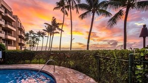 A swimming pool with a stone border, surrounded by palm trees and a building with balconies. - Affordable GEM/NewA/C, 1br/1ba w/Tropical Lanai, Steps to Ocean, LOCATION Unit 2 (Lahaina)