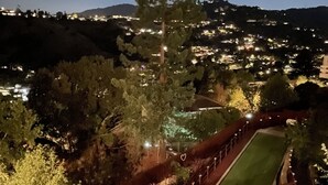 A nighttime view of a residential area with a well-lit tennis court, trees, and a distant cityscape. - Magnificent Canyon View, Huge Deck, Outdoor Dining (San Rafael)