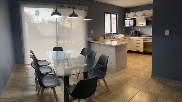 A modern kitchen with a central island, a dining area with a glass table and chairs, and a view through a large window. - Beautiful Private house with huge GARDEN (QUERETARO)