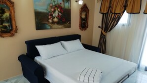 Een netjes opgemaakt bed met een witte spreideken en kussens, een donkerblauwe hoofdbord en een bloemen schilderij aan de muur.