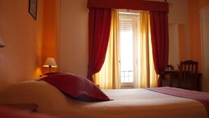 A hotel room with a bed, a lamp, a chair, and a window with curtains.
