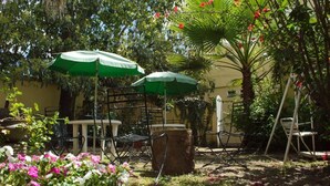 An outdoor patio area with a table and chairs, surrounded by lush greenery and flowering plants.