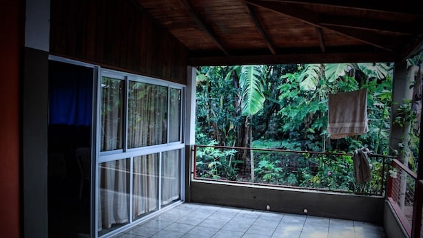 Una habitación con un amplio ventanal corredera que da a un balcón con vistas a una exuberante vegetación tropical.