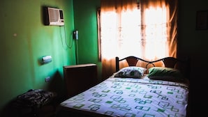 Una habitación pequeña y tenue, con una cama individual, una mesita de noche y un aire acondicionado instalado en la pared.