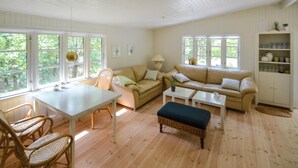 Un salón amplio con techo blanco, suelo de madera, sofá color beige, una mesa de centro blanca y un banco de mimbre.