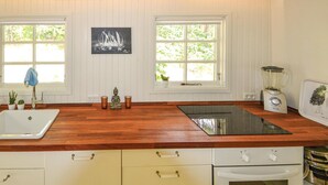 Una cocina con encimera de madera, armarios blancos, un lavamanos, una licuadora y dos ventanas con vistas a zonas verdes.