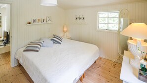 Un dormitorio con una cama grande, una mesita de noche con lámpara, un aparador, un espejo y una ventana con vistas a zonas verdes.