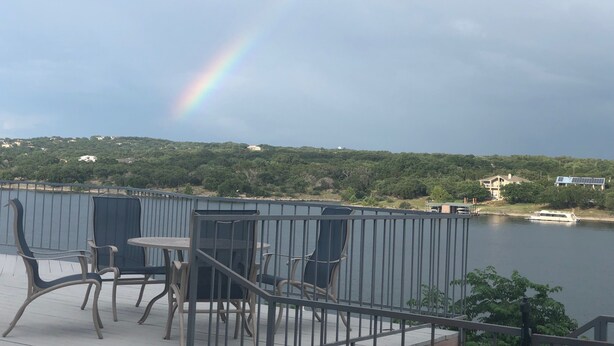 A balcony with outdoor furniture overlooking a lake, with a rainbow in the sky. - Fun N The Sun  Lake Travis Resort 105 (Spicewood)