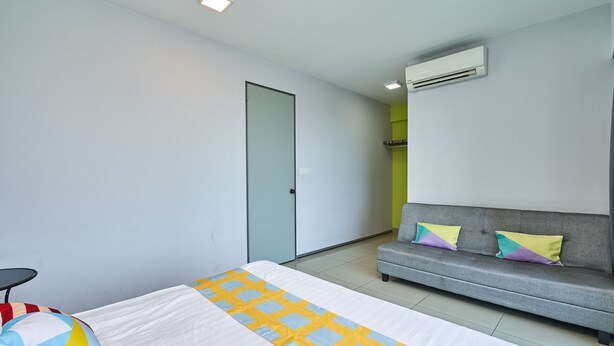 Une chambre d’hôtel moderne, équipée d’un lit, d’un canapé gris et d’un appareil de climatisation.