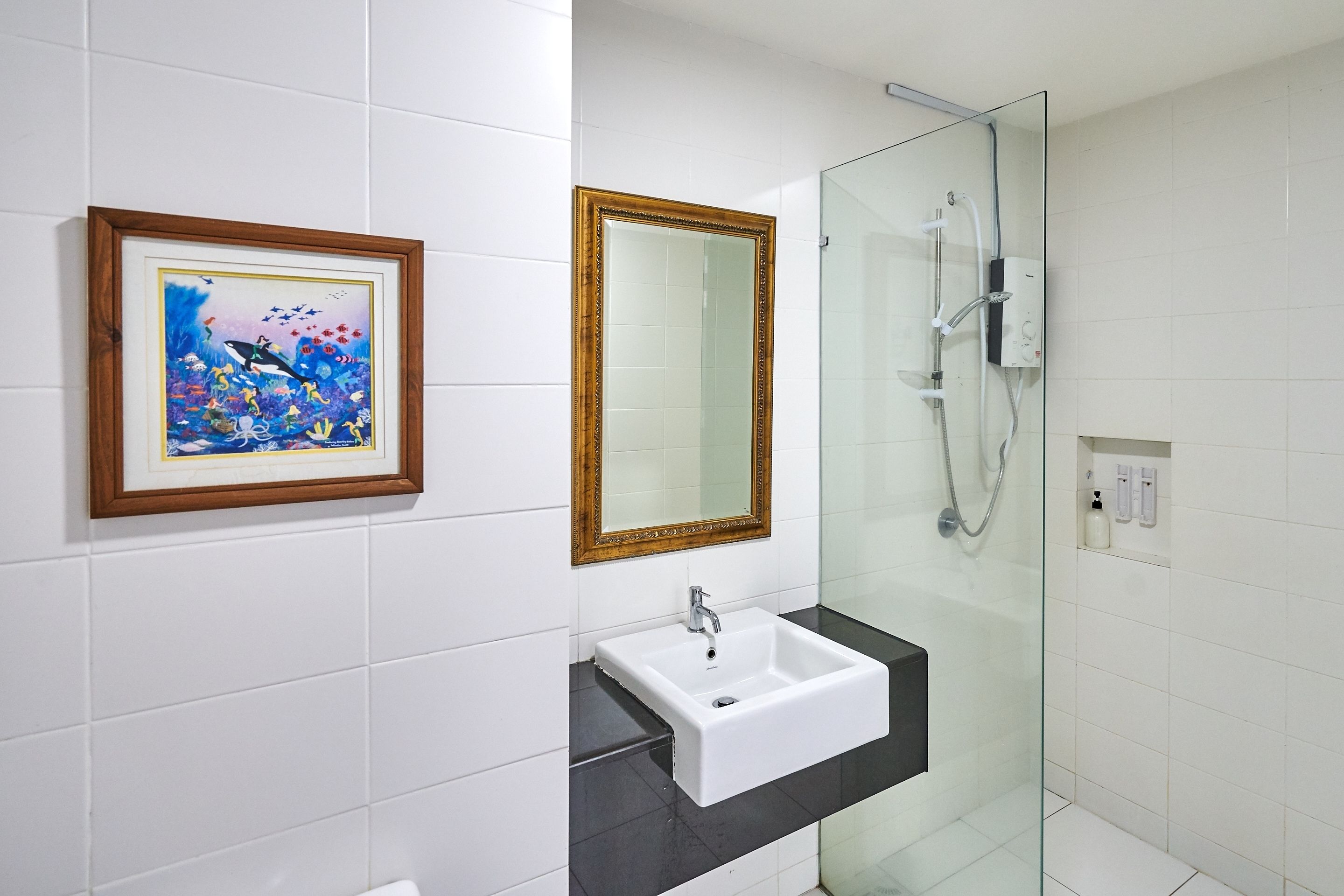 A bathroom with a white sink, a framed picture, a large mirror, and a glass-enclosed shower.