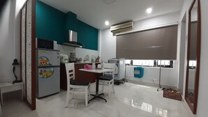 A compact kitchen with a microwave, toaster, and refrigerator, a dining area with a table and chairs, and a large window with a view. - Vuon Hong Hotel & Apartments (Da Nang)