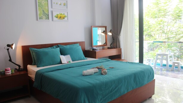 A bedroom with a bed, a nightstand, a bedside table, a mirror, and a view of the outdoors. - Vuon Hong Hotel & Apartments (Da Nang)