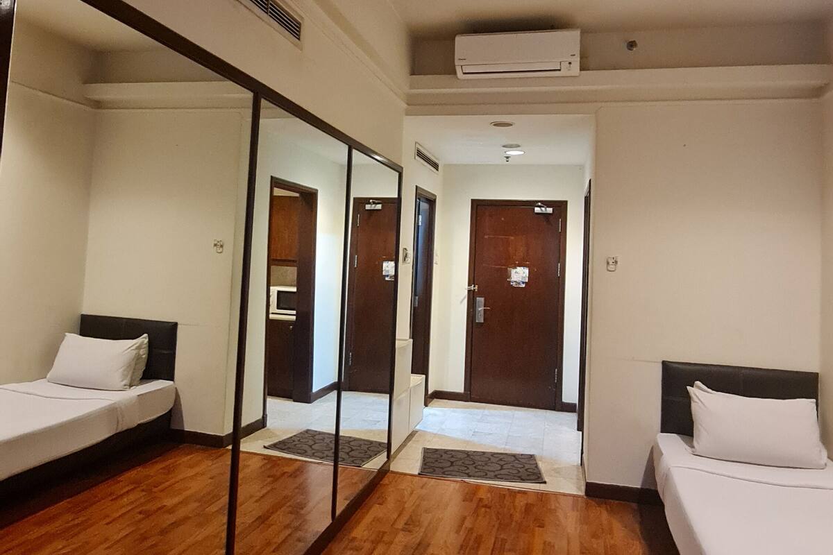 A hotel room with two beds, wooden flooring, a large mirror, and a ceiling-mounted air conditioner.