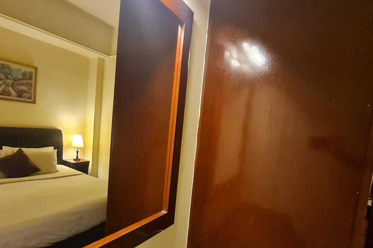 A hotel room with a bed, a nightstand, a lamp, and a door.