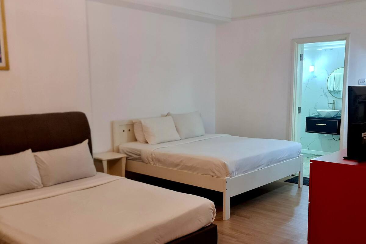 A hotel room with two beds, a TV, a small table, and a bathroom visible through an open door.