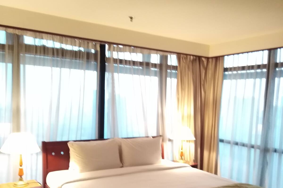 A hotel room with a bed, two bedside tables, a lamp, and a window with curtains.
