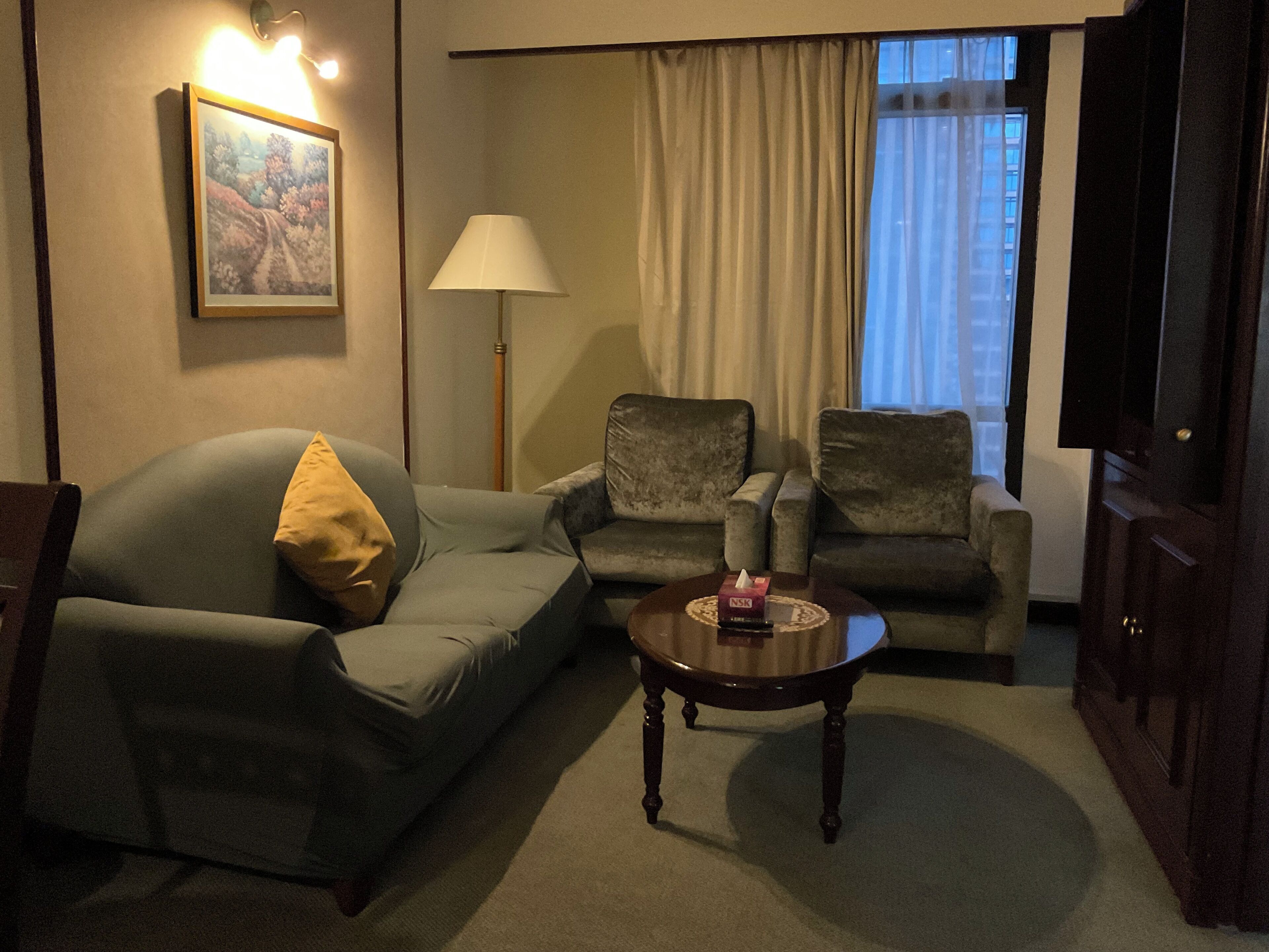 Un salon comprenant un canapé, deux fauteuils, une table basse, une lampe, un tableau et un téléviseur.