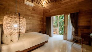 A wooden room with a bed, a hanging light fixture, a chair, and a view of greenery outside. - Rimbun Canggu Villa (Canggu)