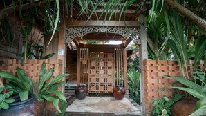A wooden entrance with a decorative gate, surrounded by potted plants and a brick wall. - Rimbun Canggu Villa (Canggu)