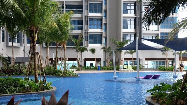 A hotel pool area with palm trees, lounge chairs, and a modern building in the background. - Comfort Home Atlantis (Malacca City)