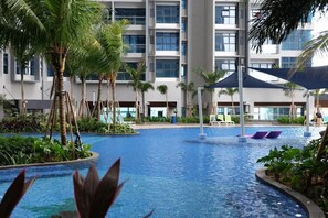 Ett hotellområde med en pool, palmer, solstolar och en modern byggnad i bakgrunden.