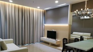 A modern living room with a sofa, a TV, a dining table, and a chandelier. - Comfort Home Atlantis (Malacca City)