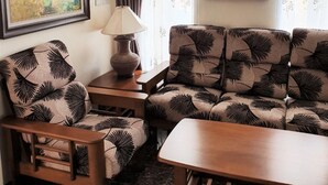 Un salon avec un canapé et un fauteuil, une table avec une lampe, un tableau et une fenêtre avec des rideaux.