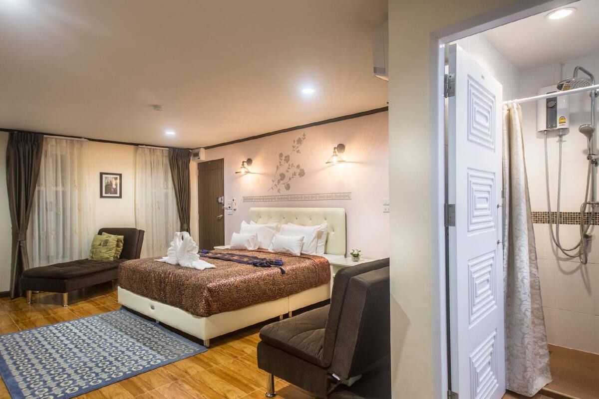 A hotel room with a bed, a chair, a small table, and a shower area.