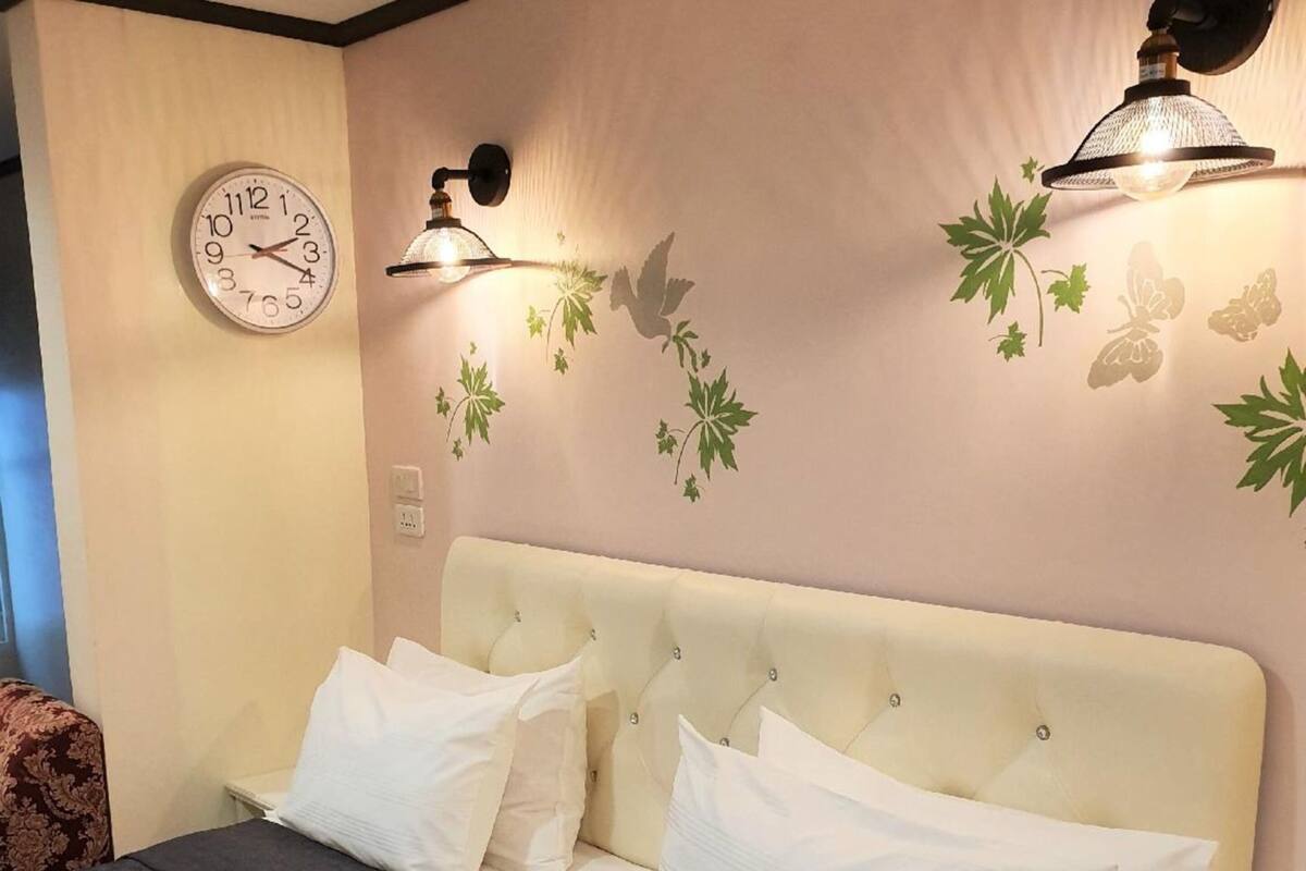 A bedroom with a bed, white pillows, a clock, and wall-mounted lights.
