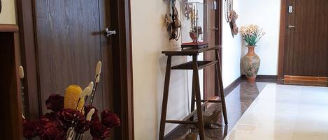 A hallway with a marble floor, wooden doors, and a wall-mounted lamp.