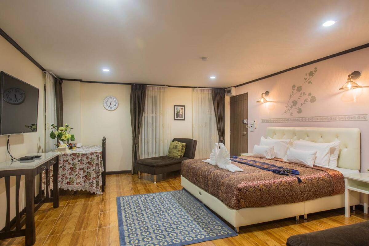 A hotel room with a bed, a desk, a chair, a clock, and a wall-mounted light fixture.