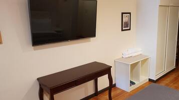 Una habitación con una televisión de pantalla plana montada en la pared, una mesita de madera, un armario blanco con toallas y un guardarropa.