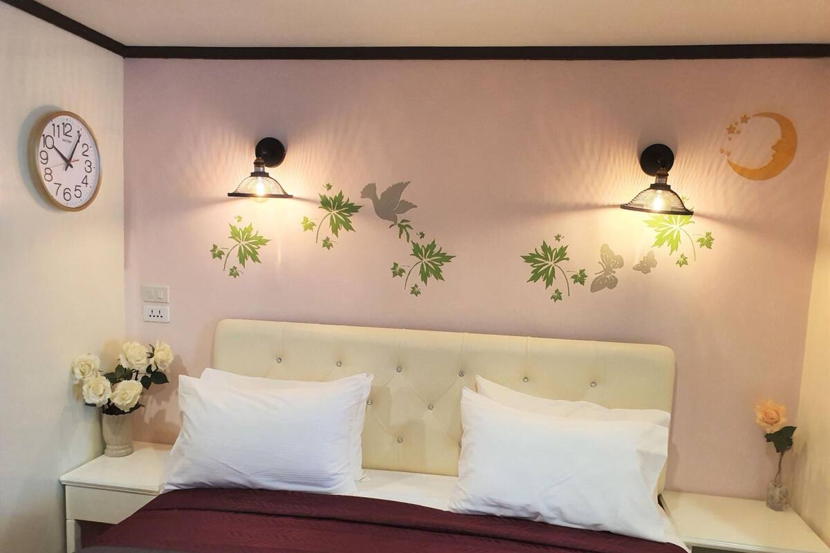 A bedroom with a bed, two nightstands, a wall clock, decorative wall stickers, and a nightlight.