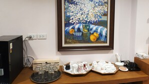Un tableau encadré représentant des fleurs et des fruits est accroché au mur, et on aperçoit un bureau sur lequel se trouvent divers objets, notamment de la verrerie et un ordinateur.