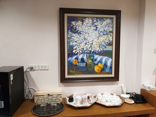 Un tableau encadré représentant des fleurs et des fruits est accroché au mur, et on aperçoit un bureau sur lequel se trouvent divers objets, notamment de la verrerie et un ordinateur.