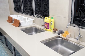 A kitchen with two sinks, a window with decorative iron bars, and various kitchen items including a yellow detergent bottle, a sponge, and a dish rack.