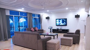 A modern living room with a large sofa, ottoman, and armchairs, a flat-screen TV, and a large window with curtains. - Cozy Villa Genting Highlands (Genting Highlands)