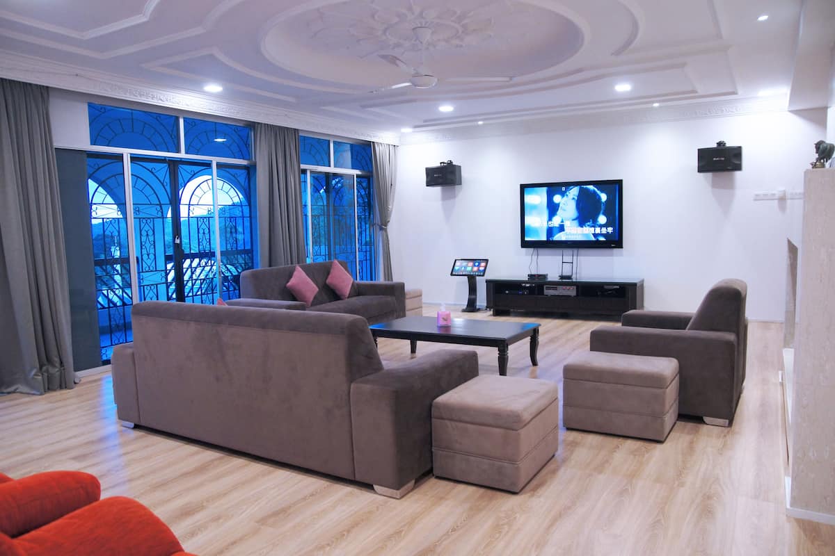 A modern living room with a large sofa, ottoman, and armchairs, a flat-screen TV, and a large window with curtains.