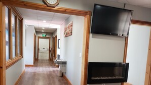 Un couloir d’hôtel avec un plancher en bois, une horloge, un téléviseur et une cheminée.