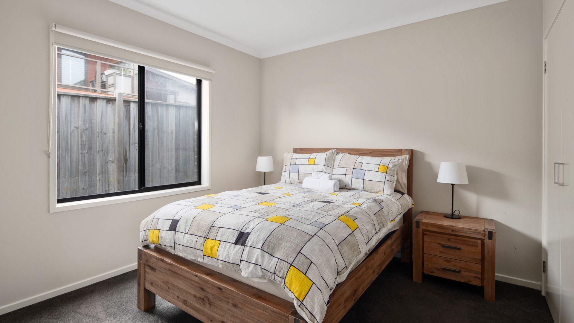 Une chambre à coucher avec un lit en bois, une table de chevet, une lampe et une fenêtre donnant sur une clôture en bois.
