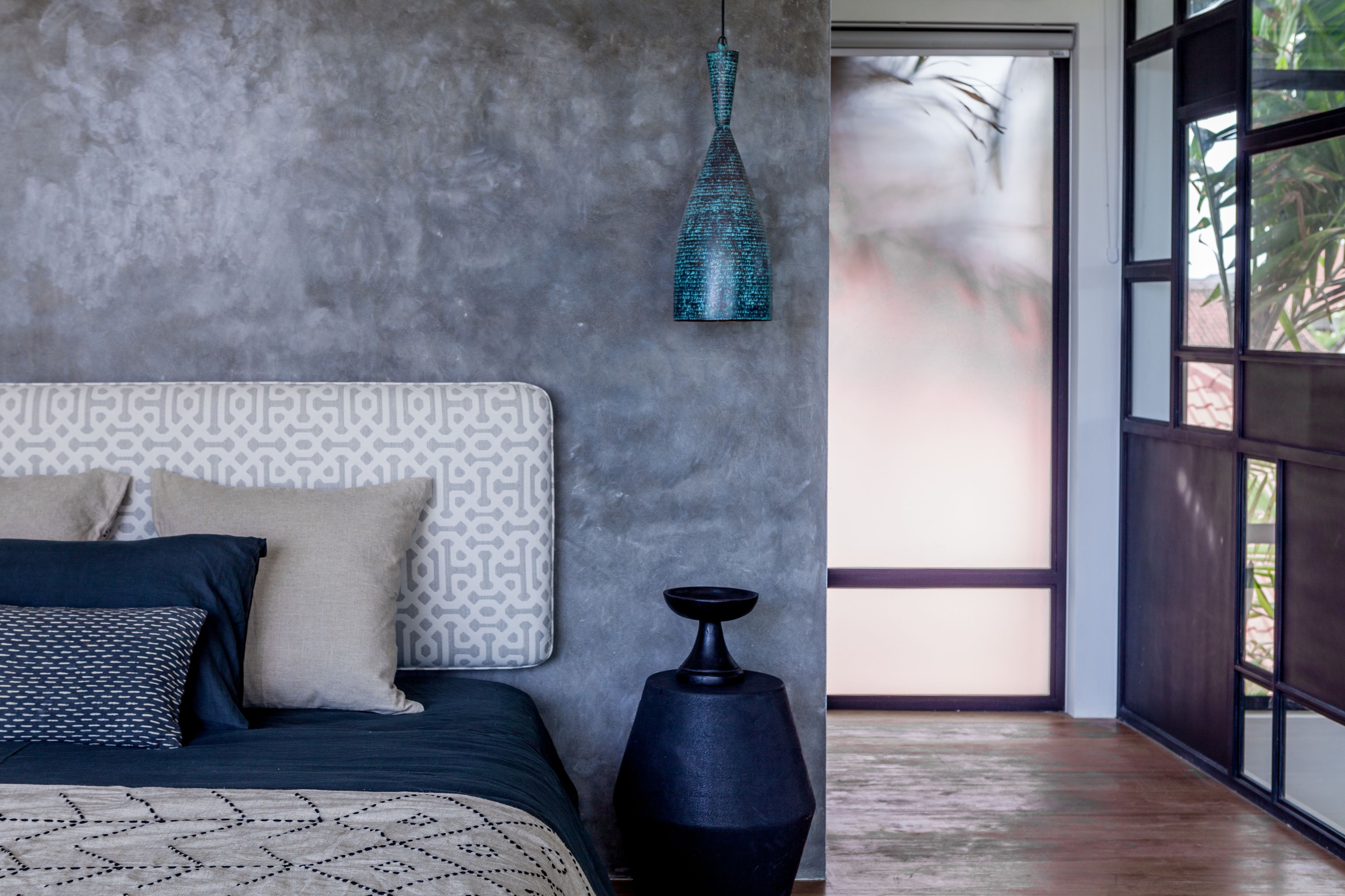 Un dormitorio moderno con un cabecero estampado, una colcha azul oscuro y un cojín de diseño geométrico.